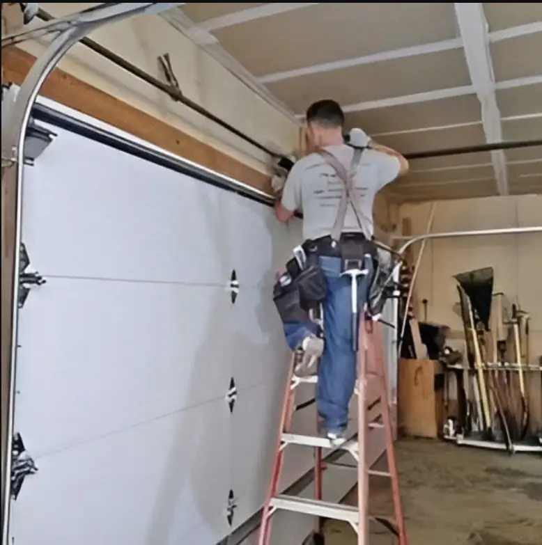 Professional technician providing garage door repair in Odessa, TX, standing on a ladder to fix a residential garage door track and spring mechanism.