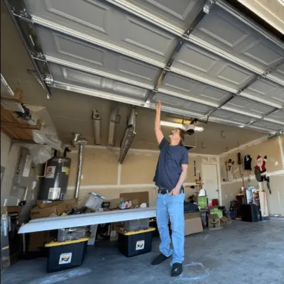 A technician inspecting a misaligned overhead garage door ceiling track and panel alignment inside a residential garage in Odessa, Texas.