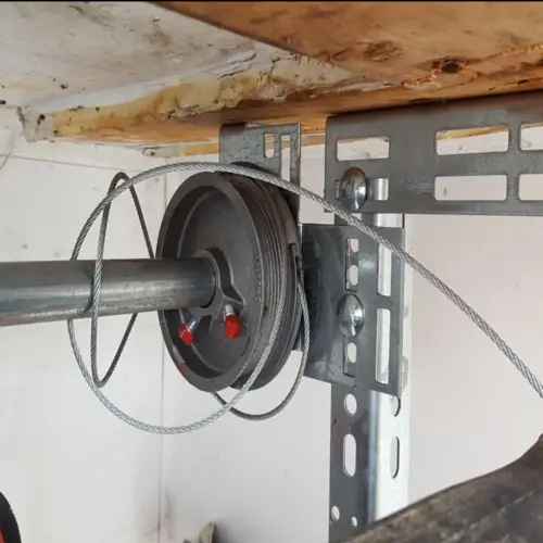 A close-up view of a tangled and broken garage door steel cable unwound from its metal torsion drum, requiring immediate replacement services in Odessa, TX.
