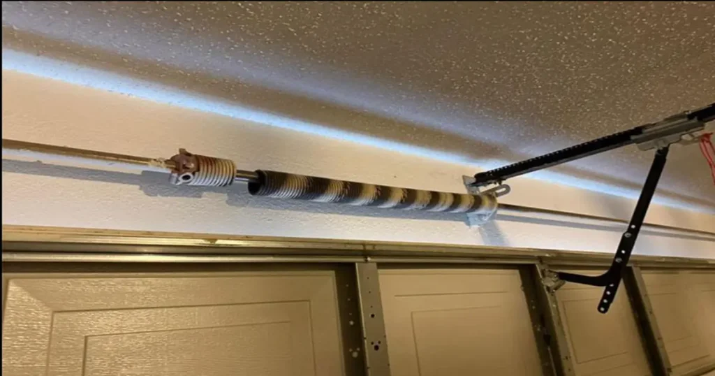 A broken garage door torsion spring showing a clear, visible gap and separation in the coil where the metal snapped above a closed residential door.