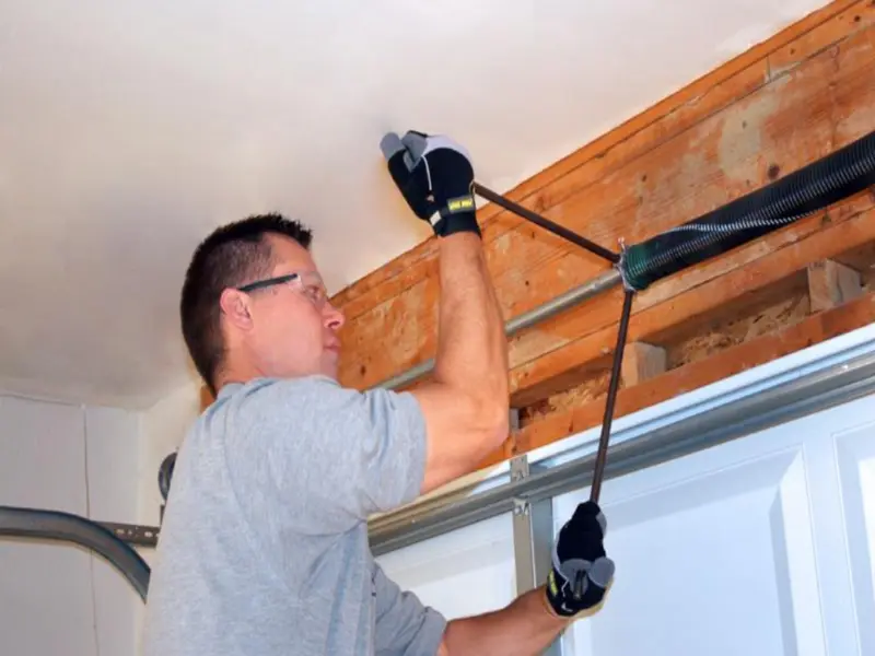 Garage Door Spring Repair Cost Odessa, TX: Professional technician safely adjusting an overhead garage door spring above a white sectional garage door.
