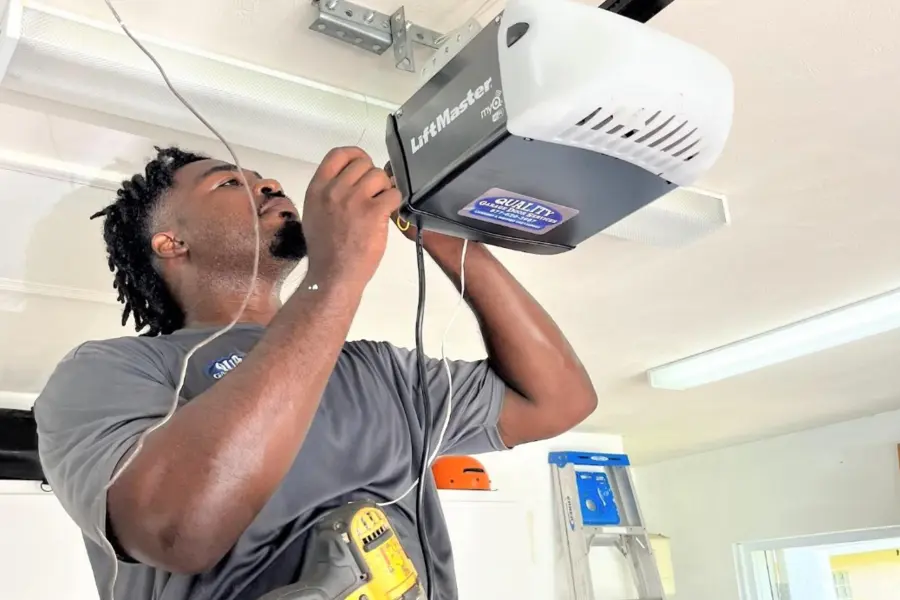 A professional technician adjusting wiring on a newly mounted LiftMaster myQ smart garage door opener system on a residential ceiling.