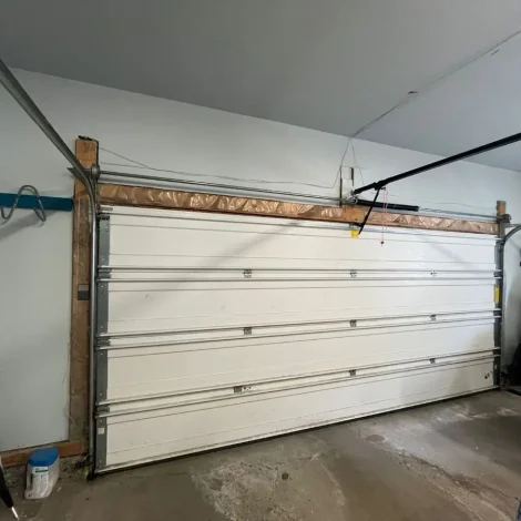 Garage Door Repair Andrews TX technician fixing a broken garage door lifting cable near the metal track and pulley system inside a residential garage.