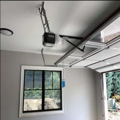 A newly installed LiftMaster belt drive garage door opener mounted to a clean garage ceiling with the sectional glass-paneled garage door partially open next to a large window during a professional garage door service in Odessa, TX.