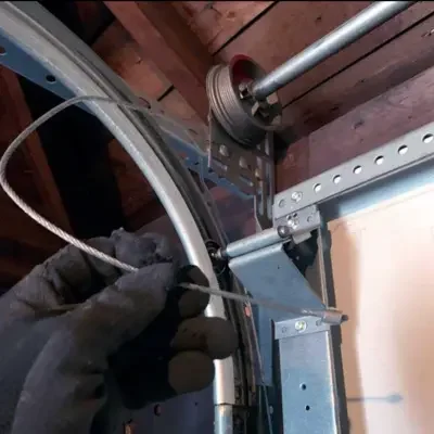 A technician inspecting a frayed lift cable and drum assembly during a routine garage door maintenance in Odessa TX.
