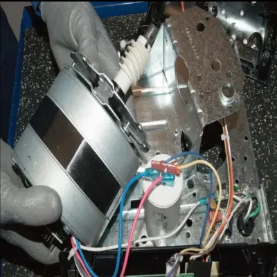 A technician holding a replacement garage door opener motor assembly near the capacitor and metal housing during a garage door opener motor repair in Odessa, TX.
