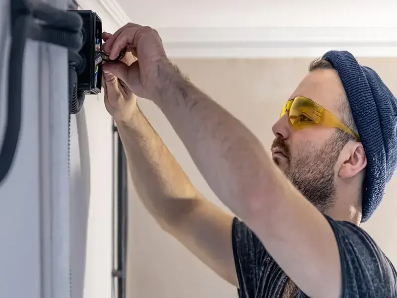 A technician fixing a motorized garage door opener system attached to the ceiling of a garage.