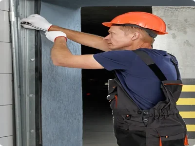A professional technician wearing a hard hat and safety gloves uses a wrench to fix a stuck garage door track during an emergency service call.