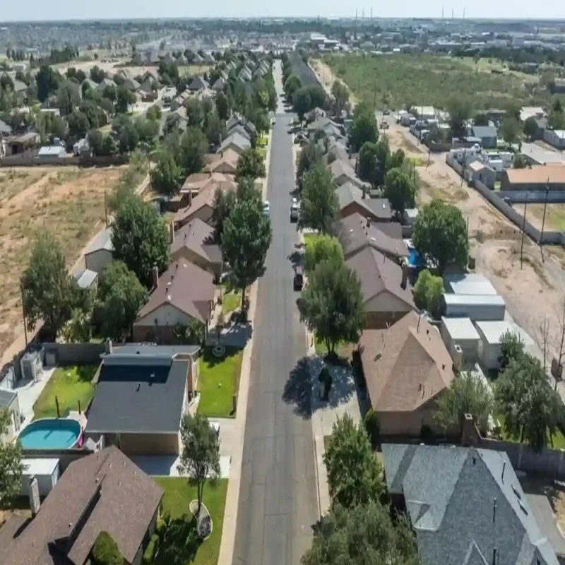 Aerial drone view of a residential neighborhood street lined with homes and garages under the intense West Texas sun, highlighting the need for regular garage door repair in Odessa, TX.