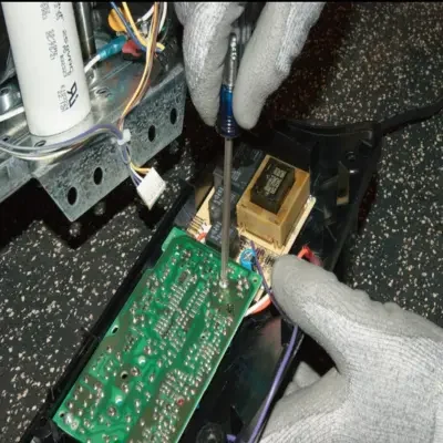 Close-up of a technician wearing safety work gloves using a screwdriver to repair or replace a green circuit logic board inside a garage door opener housing during a garage door opener repair in Odessa, TX.