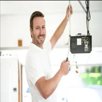 A smiling professional technician in a white shirt using a screwdriver to service an overhead automatic garage door opener during a same-day garage door opener repair in Odessa, TX.