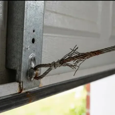 Damaged, frayed steel lifting cable attached to a garage door bracket.